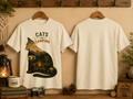 Two cream-colored t-shirts on wooden hangers, showing the front and back views. The front shirt features a graphic of a cat silhouette filled with a camping scene and the text 'CATS AND CAMPING'.